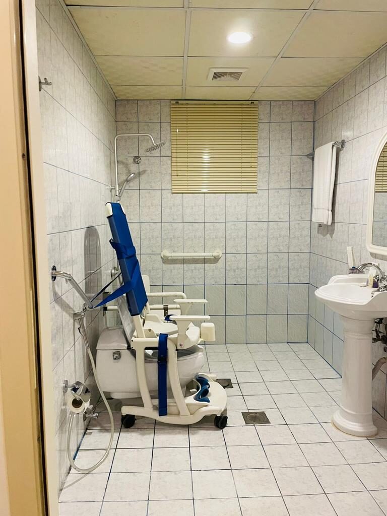 Accessible bathroom with grab bars and roll-in shower chair — حمام مهيأ بمقابض ثابتة وكرسي استحمام متحرك